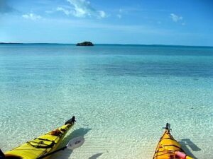 A picture of the ocean in the Bahamas. The water is a clear, bright blue, and the fronts of two kayaks poke into the bottom of the frame.